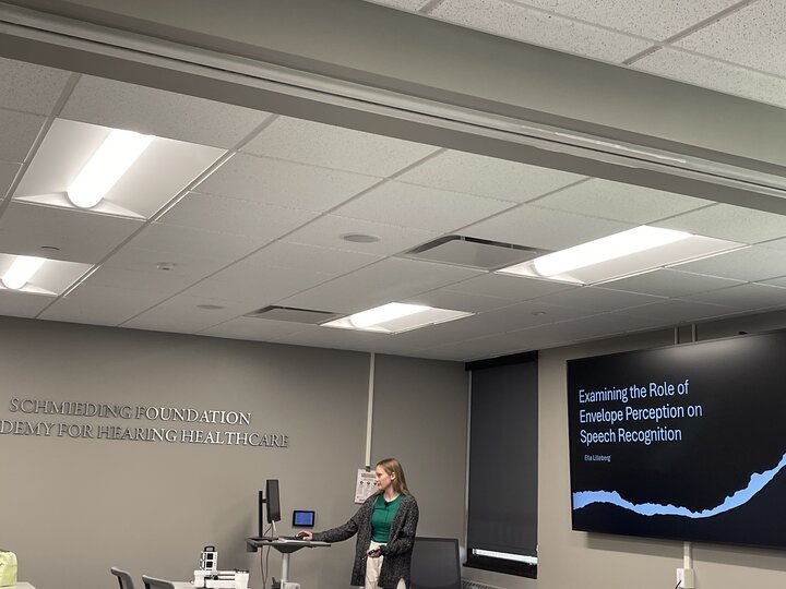 Woman presenting in a modern conference room with a slide on speech recognition displayed.